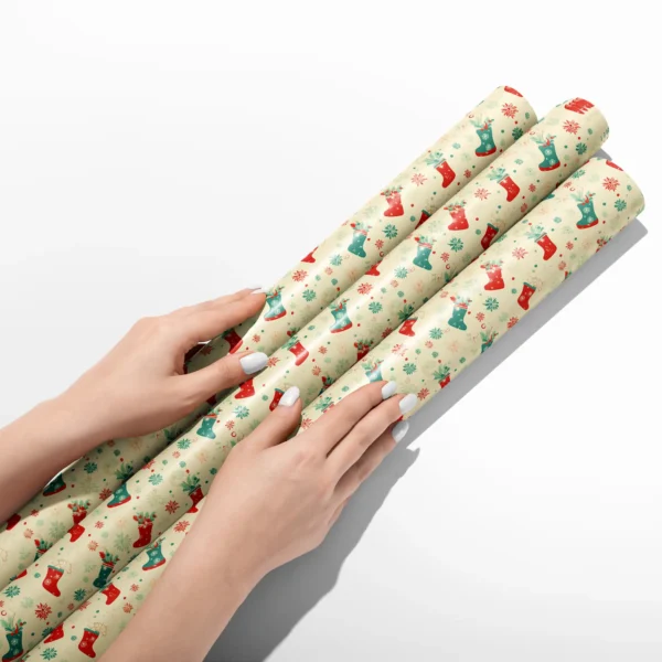 Hands smoothing three rolls of cream Christmas stocking wrapping paper on a white table
