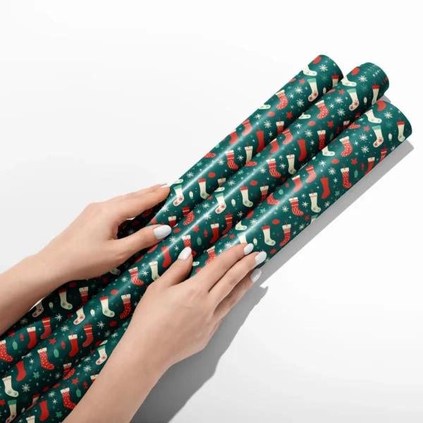 Hands smoothing three rolls of teal Christmas stocking wrapping paper on a white table
