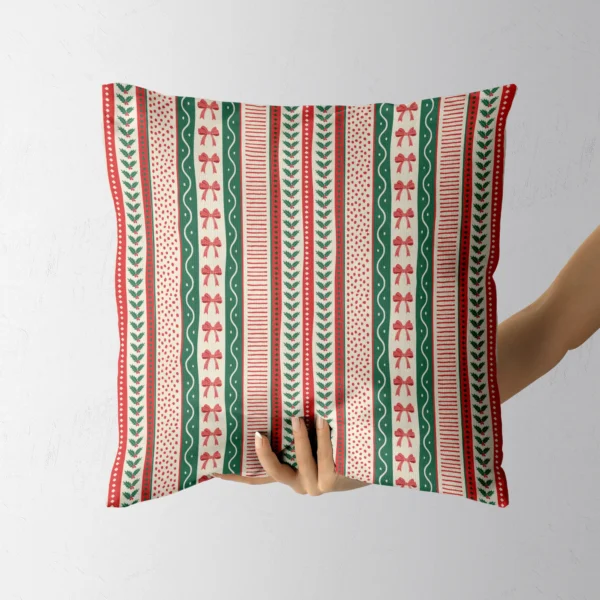 A hand holding the red and green ribbon stripe throw pillow
