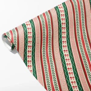 Roll of cream wrapping paper with ribbon-like bands of red bows, holly, red dots and green waves, partly unrolled on white