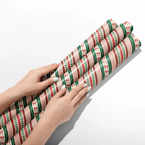 Hands smoothing three rolls of ribbon stripe wrapping paper on a white table
