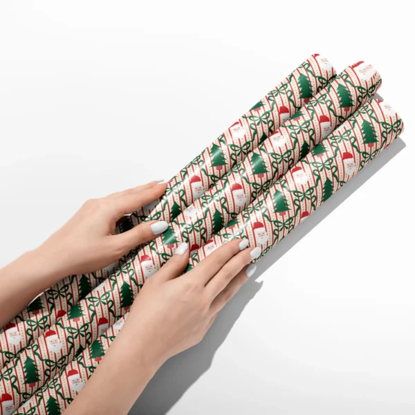 Hands smoothing three rolls of Santa trellis wrapping paper on a white table