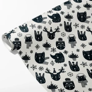 Roll of cream wrapping paper with black Scandi animal faces in party hats, snowflakes and trees, partly unrolled on white