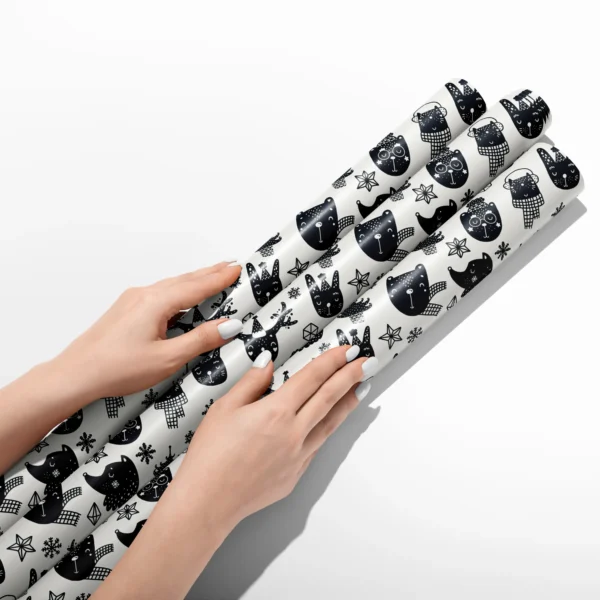 Hands smoothing three rolls of black and cream animal wrapping paper on a white table