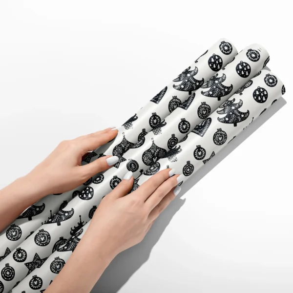 Hands smoothing three rolls of black and cream ornament wrapping paper on a white table