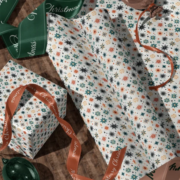 A sheet of Scandi starburst gift wrap and a wrapped box with satin ribbons on a wooden floor