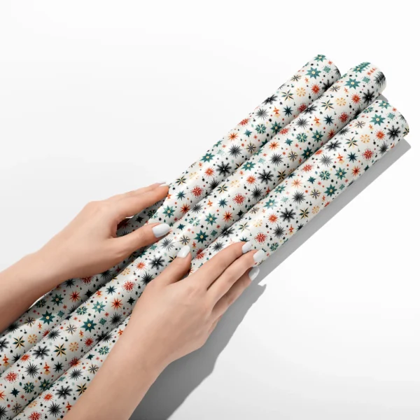 Hands smoothing three rolls of Scandi starburst wrapping paper on a white table