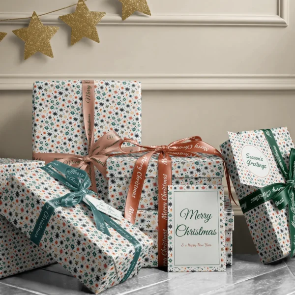 Stack of presents in Scandi starburst paper with ribbons and a Merry Christmas card by a beige wall