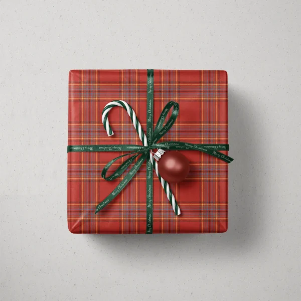 Top view of a gift in scarlet multi-stripe plaid paper with a ribbon, candy canes and a bauble