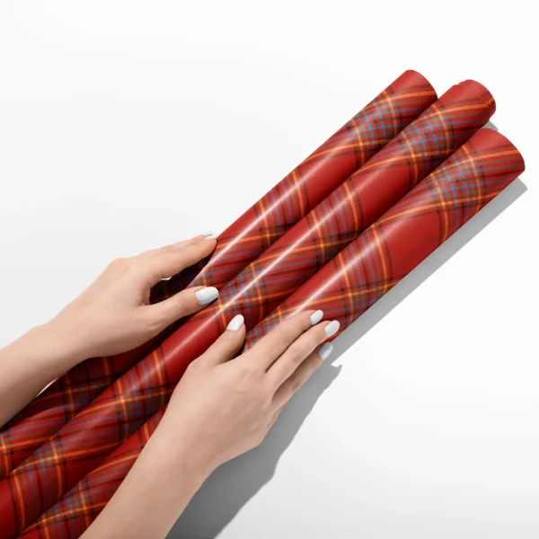 Hands smoothing three rolls of scarlet multi-stripe plaid wrapping paper on a white table