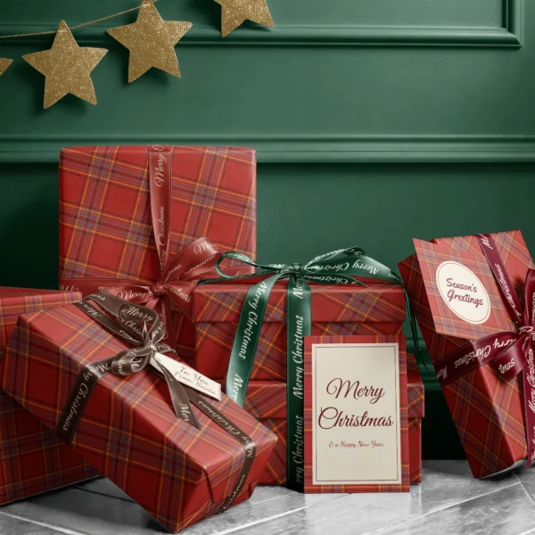 Stack of presents in scarlet multi-stripe plaid paper with ribbons and a Merry Christmas card by a dark green wall