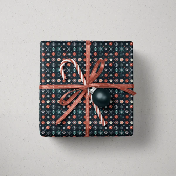 Top view of a gift in navy snowflake paper with a ribbon, a candy cane and a bauble