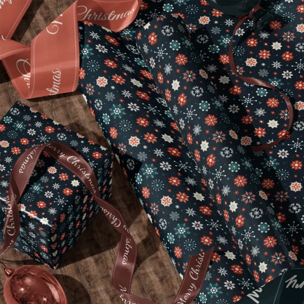 A sheet of navy snowflake gift wrap and a wrapped box with satin ribbons on a wooden floor