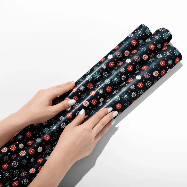 Hands smoothing three rolls of navy snowflake wrapping paper on a white table