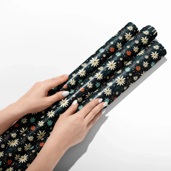 Hands smoothing three rolls of midnight starflower wrapping paper on a white table