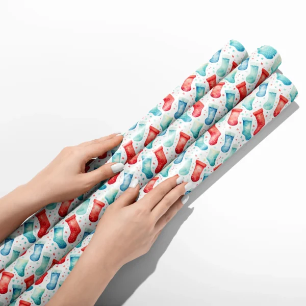 Hands smoothing three rolls of watercolor stocking wrapping paper on a white table