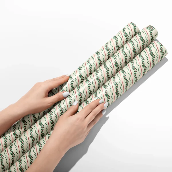Hands smoothing three rolls of berry vine wrapping paper on a white table