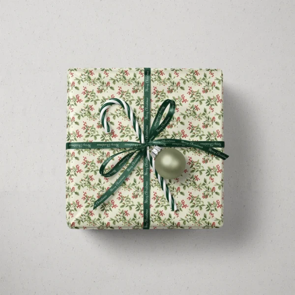 Top view of a gift in cream berry sprig paper with a ribbon, a candy cane and a bauble