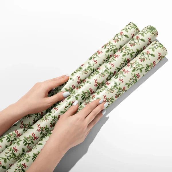 Hands smoothing three rolls of cream berry sprig wrapping paper on a white table