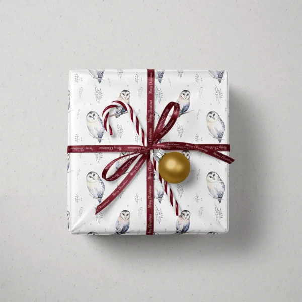 Top view of a gift in white watercolor owl paper with a ribbon, a candy cane and a bauble