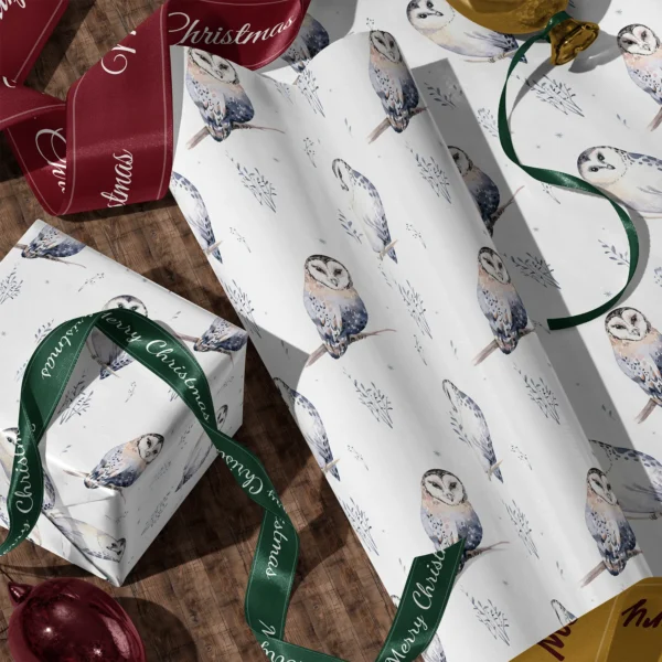 A sheet of white watercolor owl gift wrap and a wrapped box with satin ribbons on a wooden floor