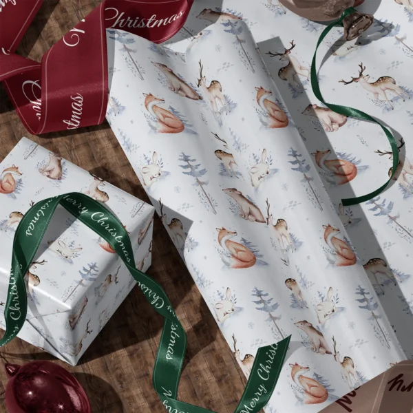 A sheet of pale blue woodland gift wrap and a wrapped box with satin ribbons on a wooden floor
