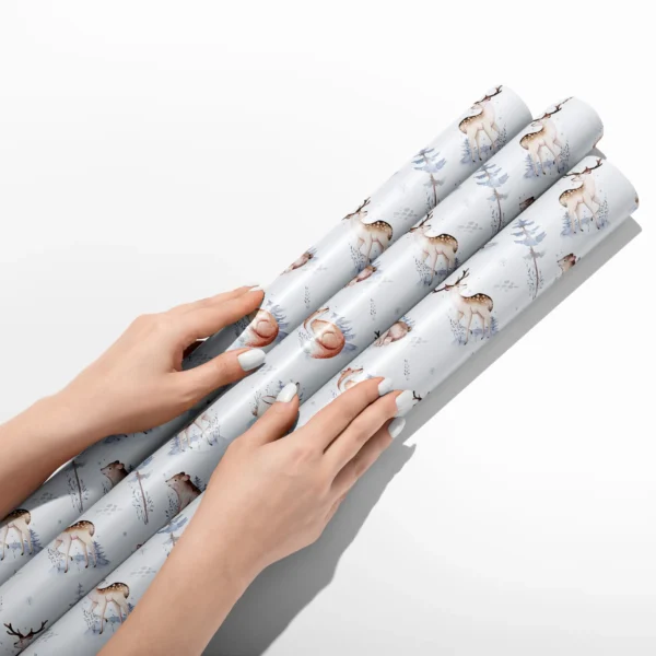 Hands smoothing three rolls of pale blue woodland wrapping paper on a white table